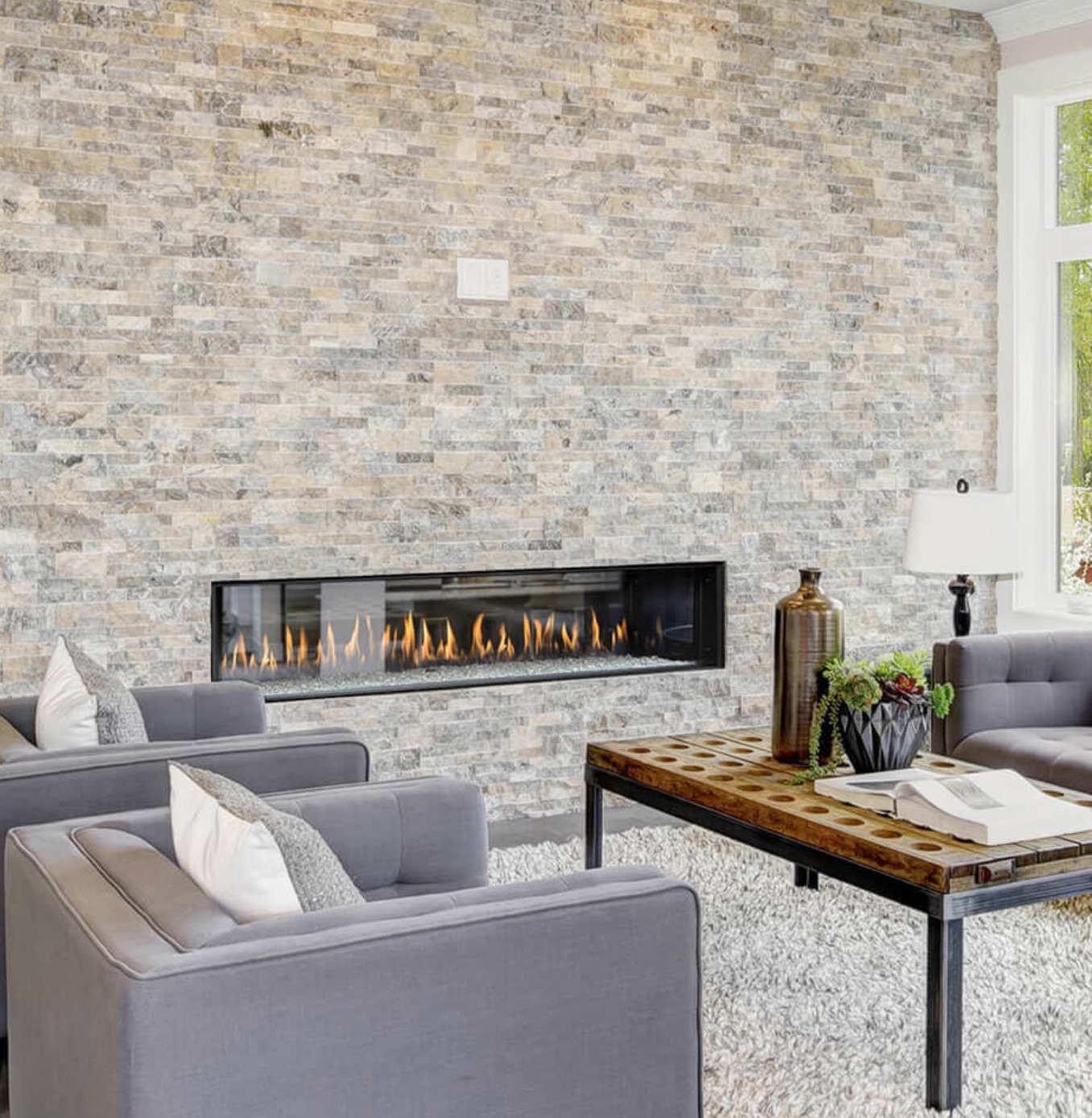 see through gas fireplace in a stacked stone beige wall in a room with modern furniture 